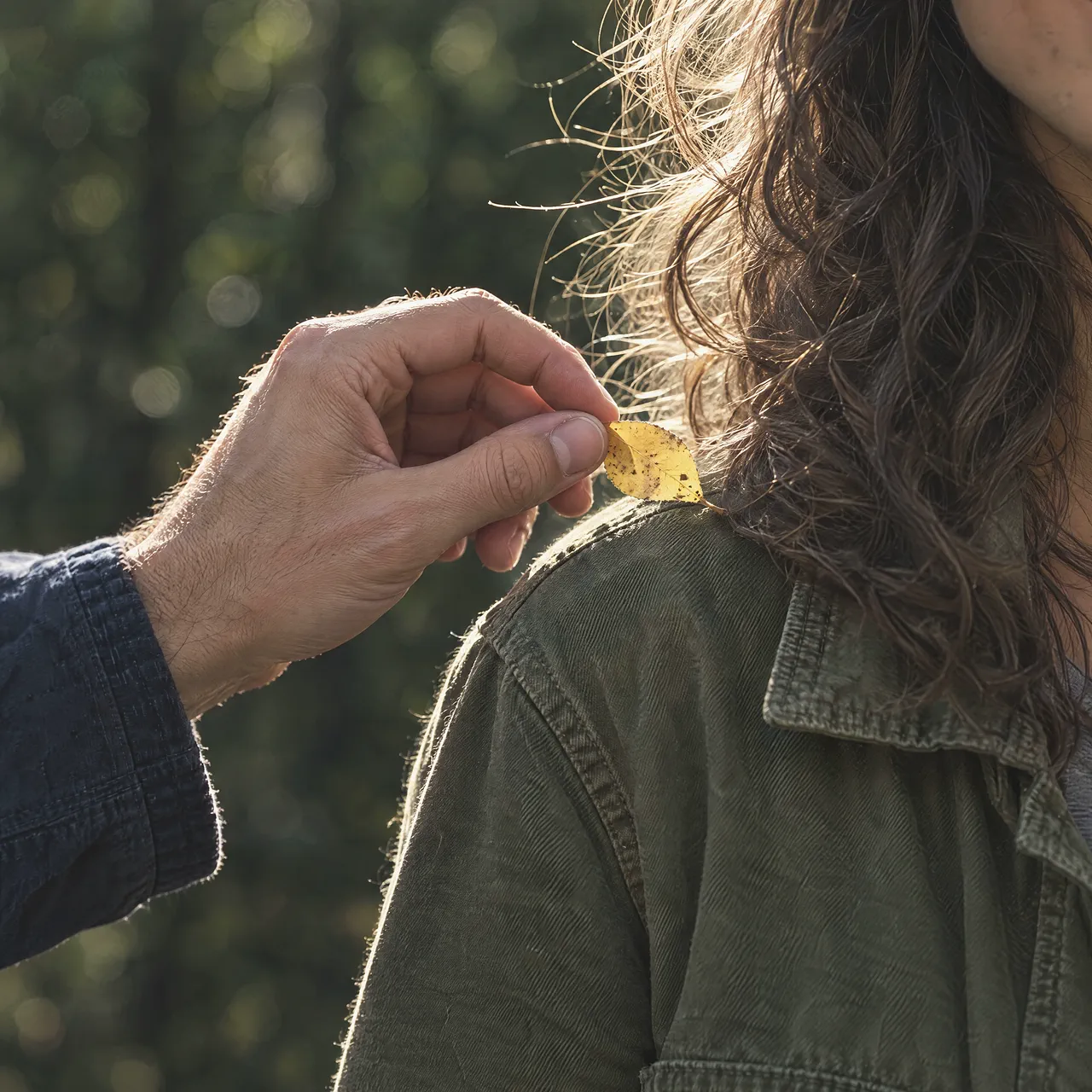 A hand lifting a yellow leaf from a friend's shoulder