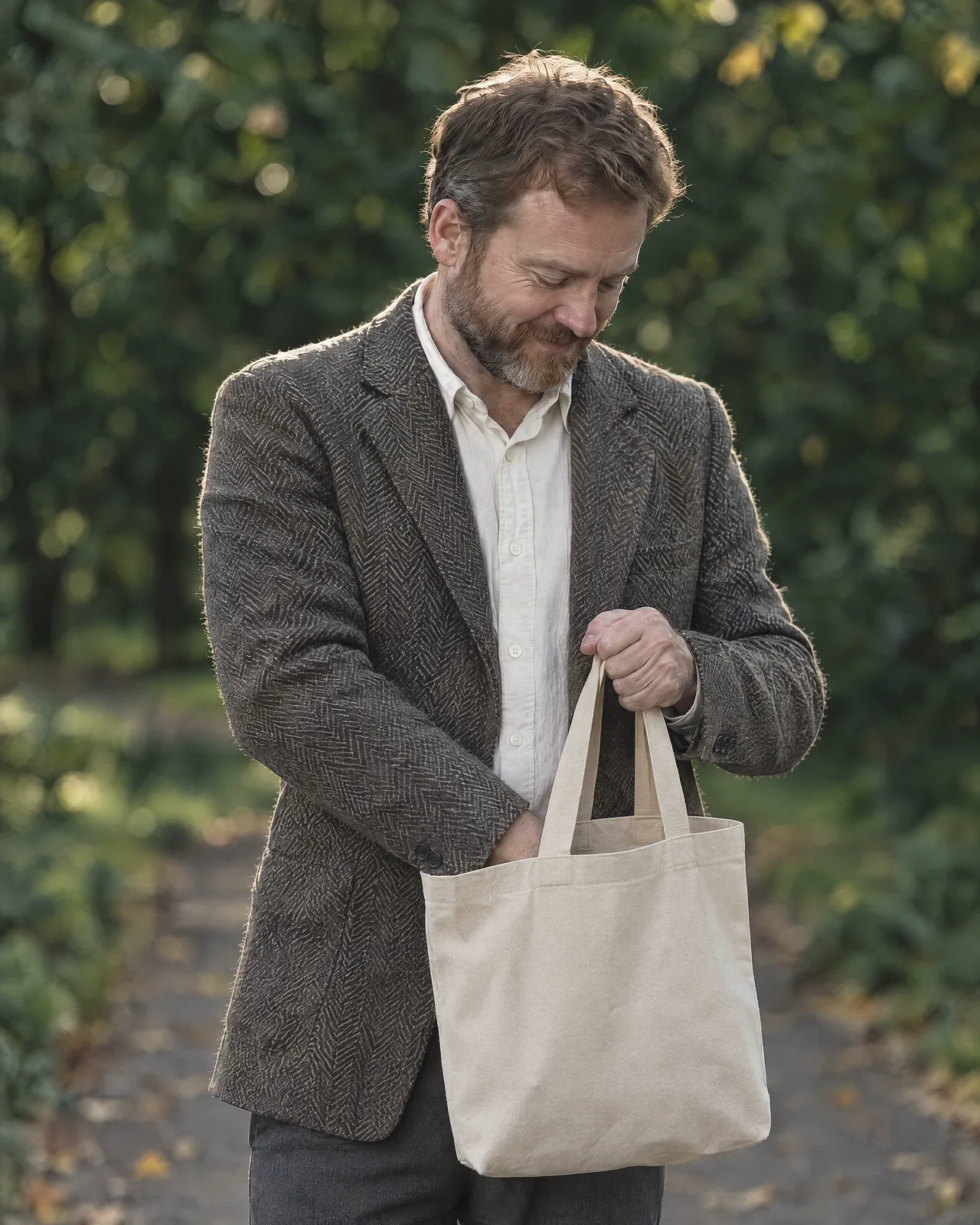 A man on a park path looking down into a canvas tote bag